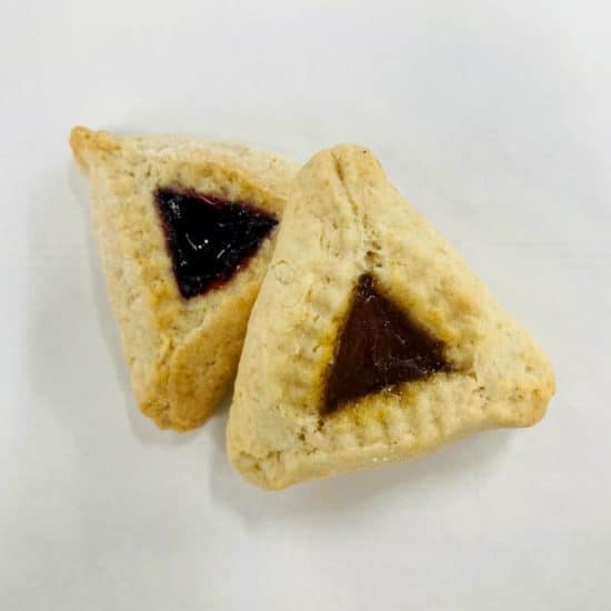 Two hamantaschen with crimped edges. The one at the upper left is filled with raspberry jam, and the lower right is filled with apricot.