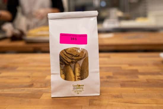 Window bag labeled "Specialty Coco Caramel - Half-Dozen 14-S" with specialty coco caramel hamantaschen visible through the window.