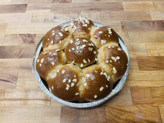 Honey Wheat Pull-Apart Rolls; 8 brown bread rolls in a pie tin with a topping of rolled oats, on a wood table top