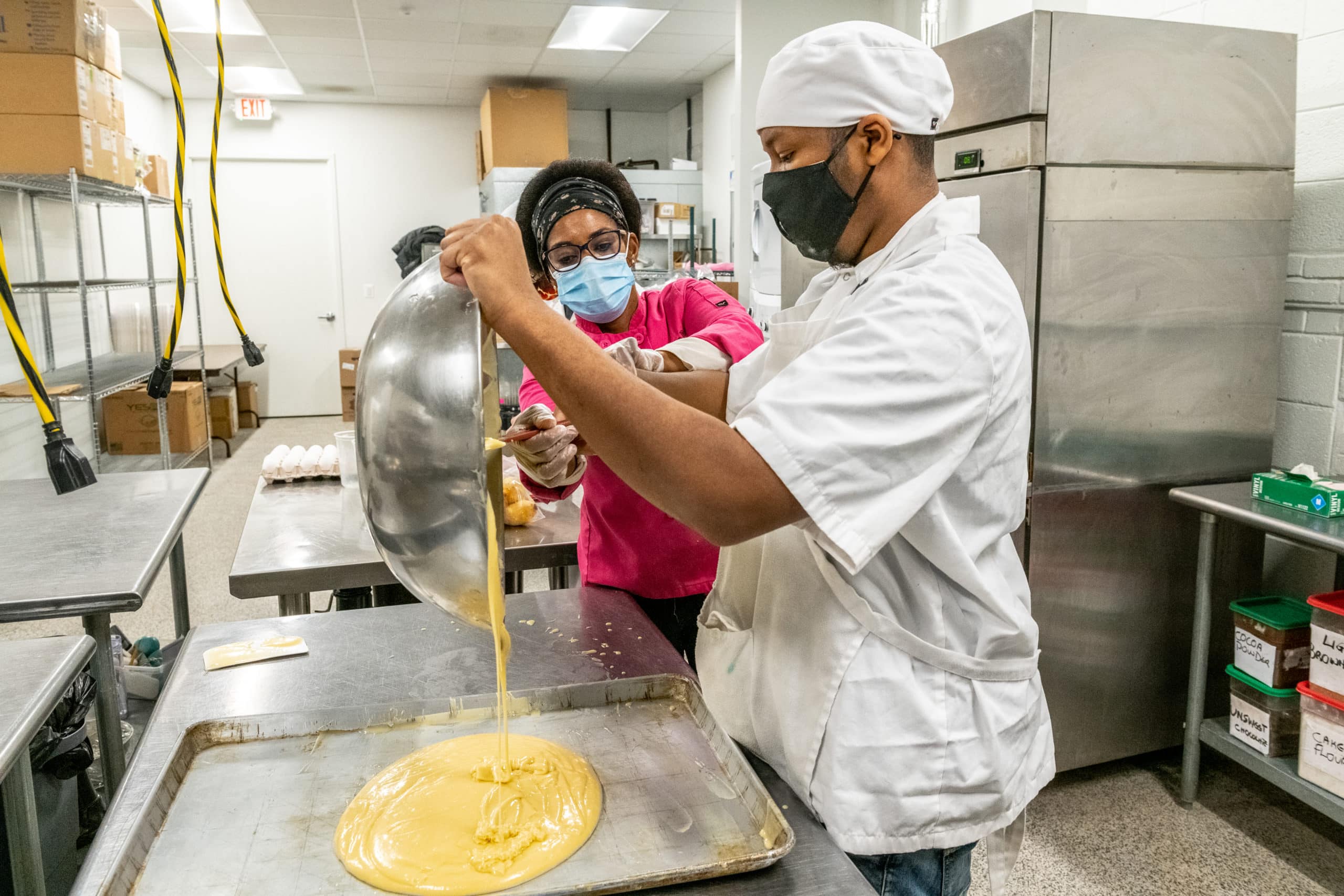 Chef instructs student as he pours cake batter into sheet pan