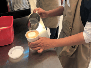 Student hands pouring milk into an espresso beverage