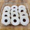 Dozen Linzer Cookies in a clear plastic clamshell on a wood countertop