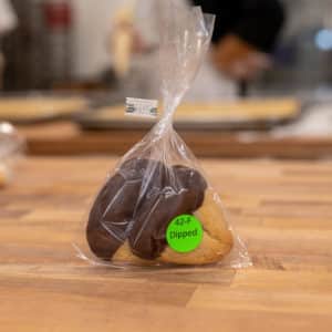 Favor bag with label "42-F Dipped" on it. Two dipped hamantaschen visible inside.