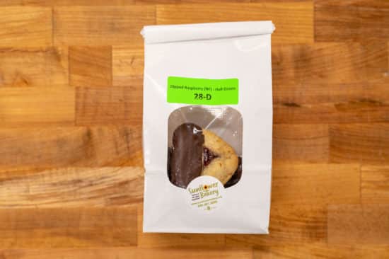 Window bag labeled "Dipped Raspberry (NF) - Half-Dozen 28-D" and traditional raspberry hamantaschen dipped in chocolate visible through the window