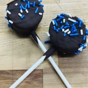 Two crossed brownie lollipops, dipped in dark chocolate, and decorated with blue and white sprinkles.