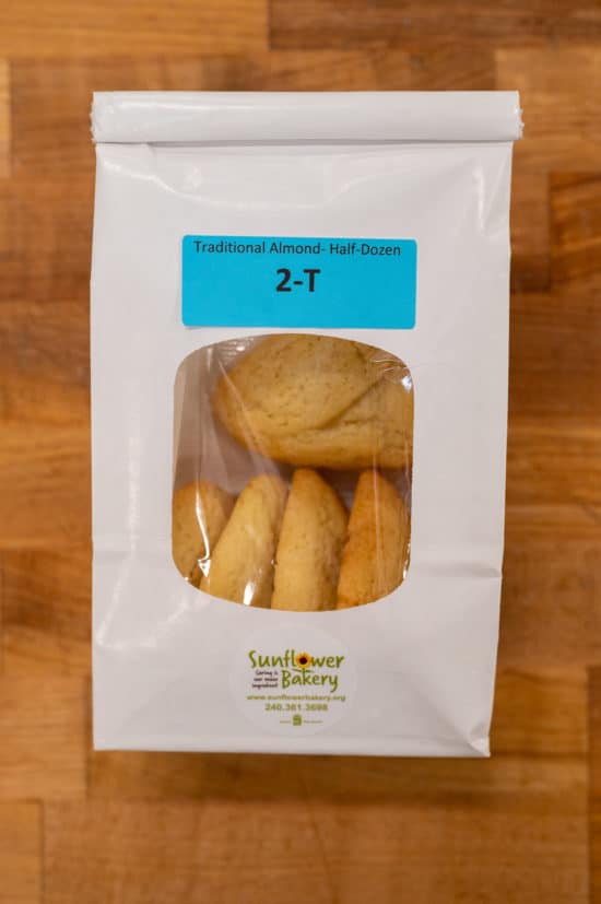 Window bag labeled "Traditional Almond - Half-Dozen 2-T" with traditional almond hamantaschen visible through the window.