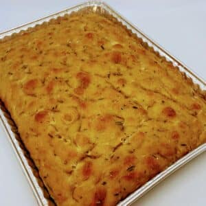 Rectangular aluminum pan with a focaccia bread with herbs mixed in and visible on the surface.