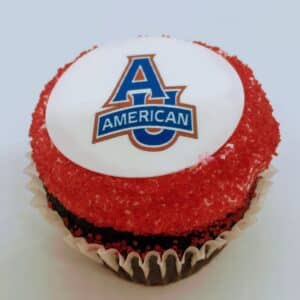 A single chocolate School Logo Cupcake, with American University Logo on a fondant disc, surrounded with red sanding sugar.
