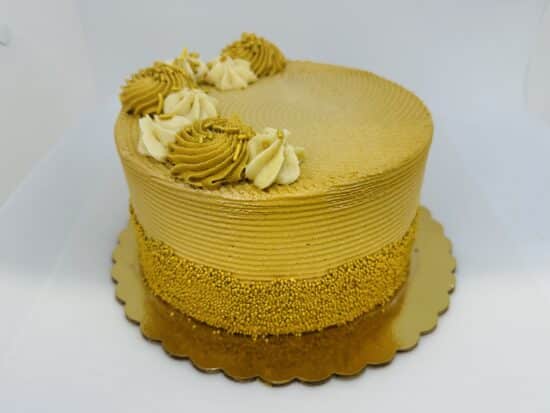 Golden brown cake with gold nonpareils decorating the lower half of the sides of the cake. Half of the top is decorated with alternating swirls of cream and gold frosting, the other space left open.