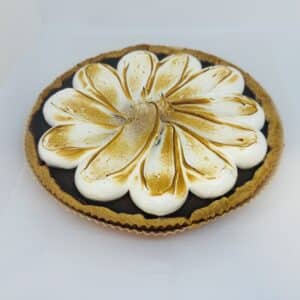 A chocolate tart and crust in a paper tart shell, with white meringue in a decorative floral shape, which is lightly toasted.