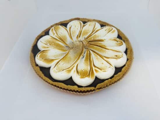 A chocolate tart and crust in a paper tart shell, with white meringue in a decorative floral shape, which is lightly toasted.