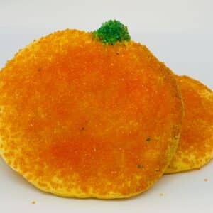 Two gluten-free rolled sugar cookies resting on a white background. The cookies are decorated with orange and green sanding sugar.