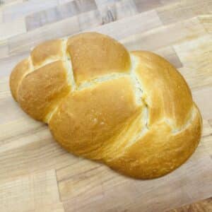 Braided loaf of challah on a wooden countertop.