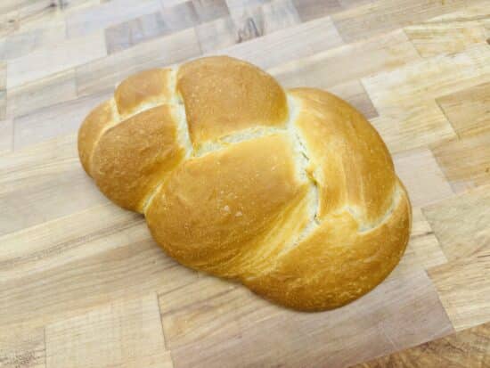 Braided loaf of challah on a wooden countertop.