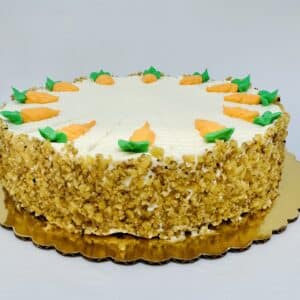 A cake with a creamy frosting top and the sides covered in walnut pieces . The top is decorated with frosting carrots, pointing inward.