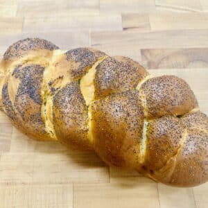 A golden brown braided challah topped with poppy seeds, on a wooden countertop.