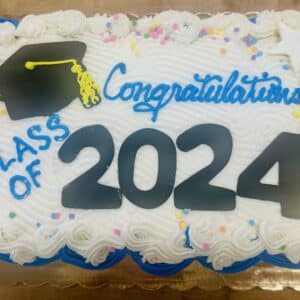 Top down view of a cupcake cake with white frosting and a a white border and sprinkles. A combination of black fondant and blue and yellow frosting represent a graduation cap, and say "Congratulations Class of 2024".
