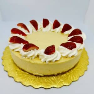 8 inch cheesecake with a cookie crust on a golden cake circle. Decorated with whipped cream and fresh strawberries.