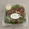 A clear plastic box containing kale leaves topped with roased vegetables, with a cup of dressing on the side.