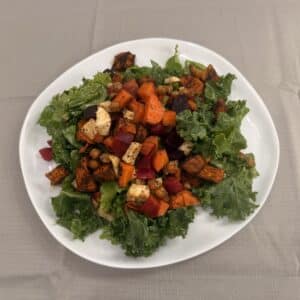 Plate of kale topped with roasted vegetables tossed in dressing.