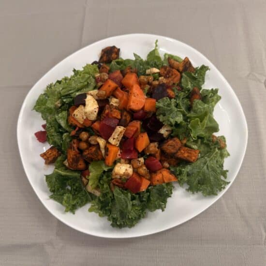 Plate of kale topped with roasted vegetables tossed in dressing.