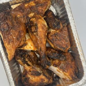 Aluminum pan with a whole chicken covered in BBQ sauce and cut into 8 pieces.