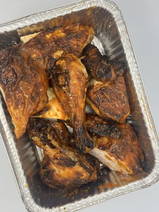 Aluminum pan with a whole chicken covered in BBQ sauce and cut into 8 pieces.