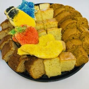 Black platter with sliced apple cake, glazed lemon poppy cake, and honey cake, decorated with Rosh Hashanah themed sugar cookies.