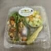 Clear plastic box containing a roasted veggie wrap, container of diced fruit, and a pickle spear.
