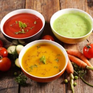 Three bowls of colorful soup, surrounded by vegetables