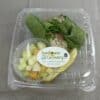 A clear plastic box containing a tuna wrap, a cup of diced fruit, and a pickle spear.