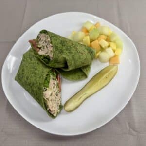 A tuna wrap, diced fruit, and a pickle spear on a plate.