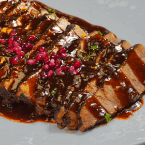 Close view of pomegranate glazed brisket on a white plate.