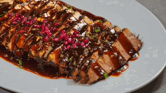 Close view of pomegranate glazed brisket on a white plate.