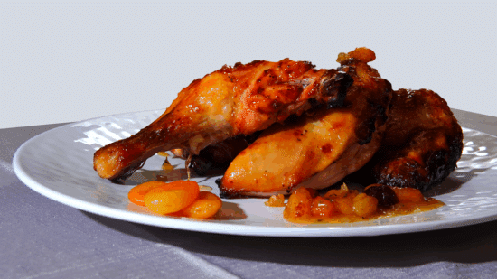 Apricot chicken on a white plate, on a table cloth and a light background.