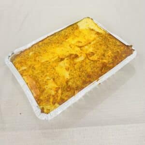 Potato kugel in an aluminum pan on a cream table cloth.