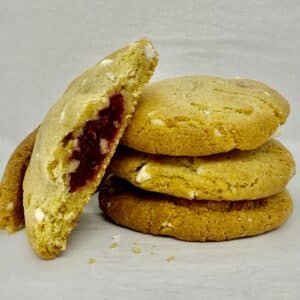 Stack of cookies with white chocolate chunks. One is broken open to show cranberry center.